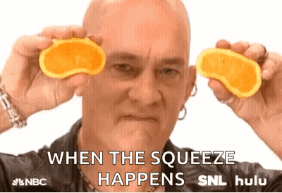 A Bald Man Is Holding Two Slices Of Orange In Front Of His Eyes And Says When The Squeeze Happens . GIF