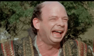 A Bald Man Is Laughing With His Eyes Closed While Wearing A Robe . GIF