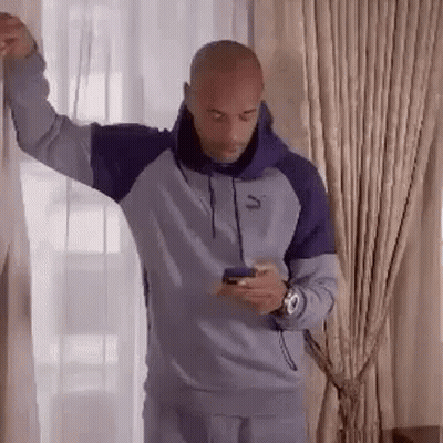 A Bald Man Is Leaning Against A Wall While Looking At His Phone . GIF