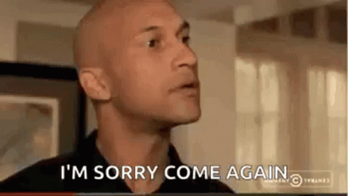 A Bald Man Is Saying `` I 'M Sorry Come Again '' While Standing In A Living Room . GIF