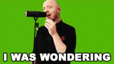 A Bald Man Is Singing Into A Microphone With The Words `` I Was Wondering '' Written On The Screen Behind Him . GIF