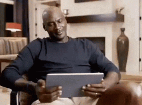 A Bald Man Is Sitting In A Chair Looking At A Tablet Computer . GIF