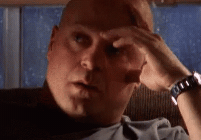 A Bald Man Is Sitting In A Chair With His Hand On His Forehead And A Watch On His Wrist . GIF