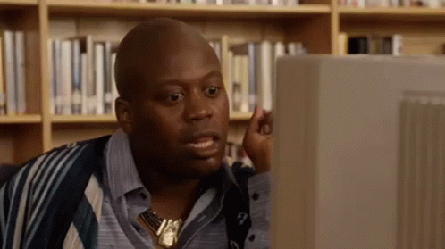 A Bald Man Is Sitting In Front Of A Computer Screen In A Library . GIF