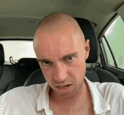 A Bald Man Is Sitting In The Driver 'S Seat Of A Car Making A Funny Face . GIF