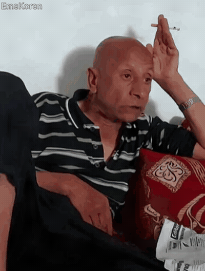 A Bald Man Is Smoking A Cigarette While Sitting On A Couch GIF