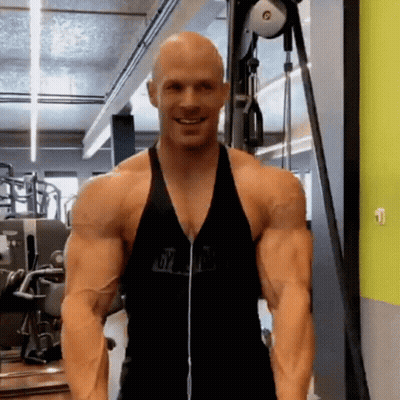 A Bald Man Is Standing In A Gym Wearing Headphones And A Black Tank Top . GIF