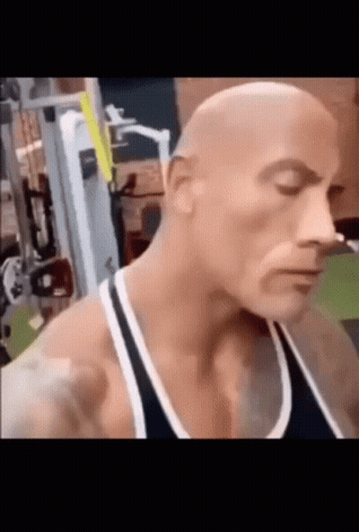 A Bald Man Is Standing In A Gym With His Eyes Closed And A Black Tank Top On . GIF
