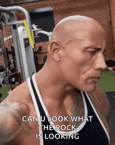 A Bald Man Is Standing In A Gym With The Words `` Can U Look What The Rock Is Looking '' On His Face . GIF