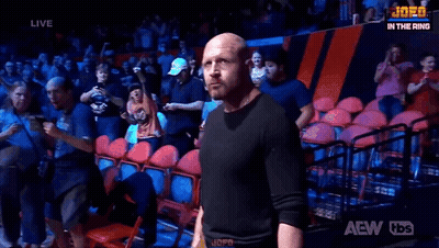 A Bald Man Is Standing In Front Of A Crowd In A Wrestling Ring . GIF