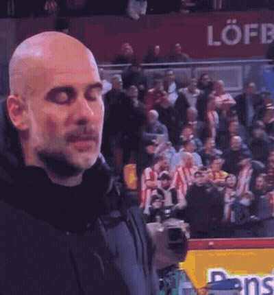 A Bald Man Is Standing In Front Of A Crowd Of People Watching A Soccer Game . GIF