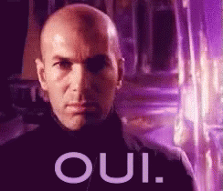 A Bald Man Is Standing In Front Of A Purple Background With The Word Oui Written On It . GIF