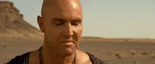 A Bald Man Is Standing In The Desert With His Eyes Closed And A Serious Look On His Face . GIF