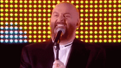 A Bald Man Singing Into A Microphone With A Beard GIF