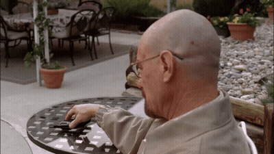 A Bald Man Sits At A Table With A Cell Phone GIF
