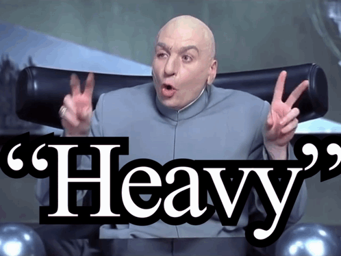A Bald Man Sitting In A Chair With The Word Heavy On The Bottom Right GIF
