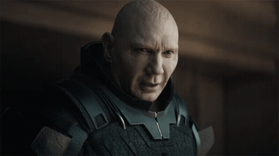 a bald man wearing a black armored suit looks at the camera