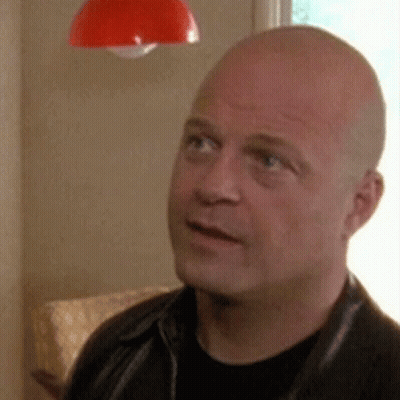 A Bald Man Wearing A Black Shirt And A Black Leather Jacket Is Looking Up At Something . GIF