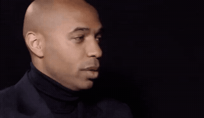 A Bald Man Wearing A Black Turtleneck Is Smiling . GIF