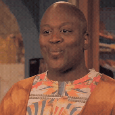 A Bald Man Wearing A Floral Shirt And A Cardigan Is Smiling . GIF