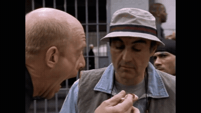 A Bald Man Wearing A Hat Is Talking To Another Man GIF
