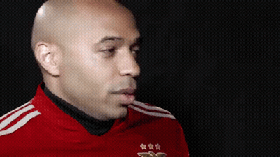 A Bald Man Wearing A Red Shirt With Three Stars On It Is Looking At The Camera . GIF