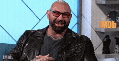 A Bald Man Wearing Glasses And A Black Leather Jacket Is Sitting In Front Of A Sign That Says Imdb GIF