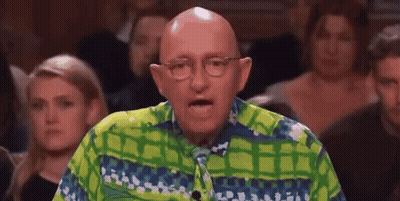 A Bald Man Wearing Glasses And A Green And Blue Shirt Is Speaking In Front Of A Crowd . GIF