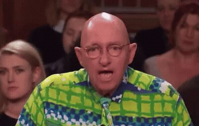 A Bald Man Wearing Glasses And A Green And Blue Shirt Is Speaking In Front Of A Crowd . GIF