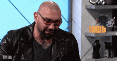 A Bald Man Wearing Glasses And A Leather Jacket Stands In Front Of A Sign That Says Imdb On It GIF