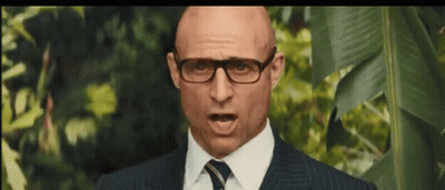 A Bald Man Wearing Glasses And A Suit And Tie Is Making A Funny Face . GIF