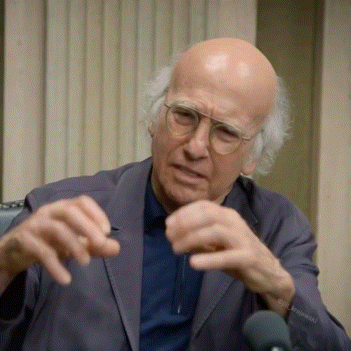 A Bald Man Wearing Glasses And A Suit Is Sitting In Front Of A Microphone With His Hands Outstretched GIF