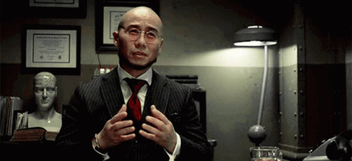 A Bald Man Wearing Glasses And A Suit Is Talking GIF
