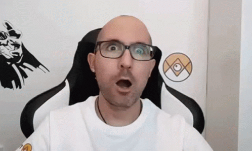 A Bald Man Wearing Glasses And A White Shirt Is Sitting In A Gaming Chair . GIF
