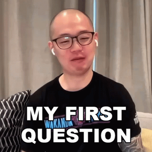 A Bald Man Wearing Glasses And Earbuds Says My First Question GIF