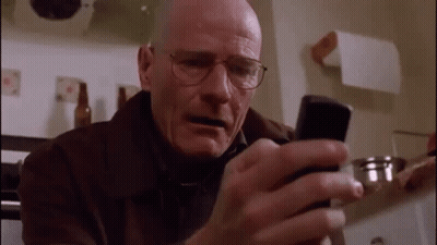 A Bald Man Wearing Glasses Is Looking At A Cell Phone In A Kitchen . GIF