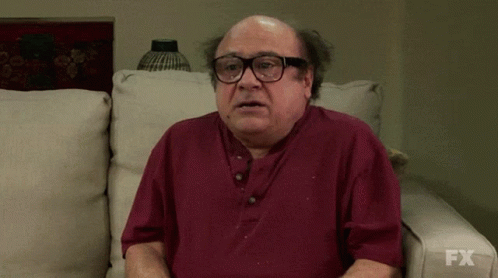A Bald Man Wearing Glasses Is Sitting On A Couch With Fx Written On The Bottom Of His Shirt GIF