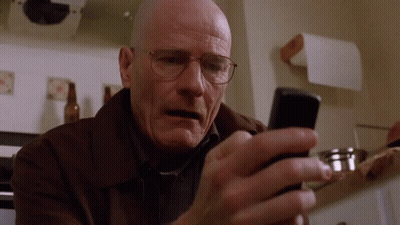 A Bald Man Wearing Glasses Looks At His Cell Phone GIF