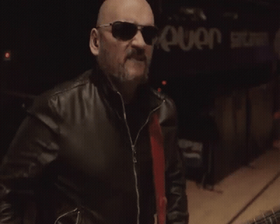 A Bald Man Wearing Sunglasses And A Leather Jacket Is Playing A Guitar GIF