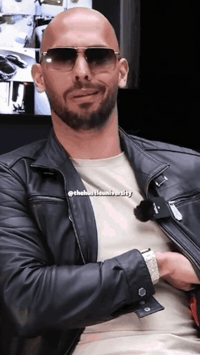 A Bald Man Wearing Sunglasses And A Leather Jacket With The Hustle University Written On His Shirt GIF