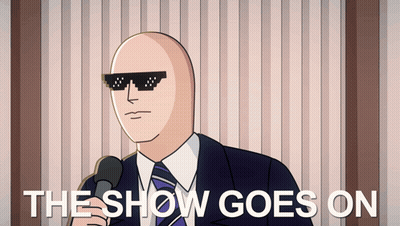 A Bald Man Wearing Sunglasses Is Holding A Microphone And The Show Goes On Is Written Below Him GIF