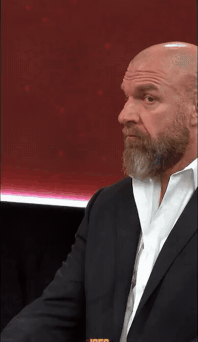 A Bald Man With A Beard And Glasses Is Wearing A Suit And Tie . GIF