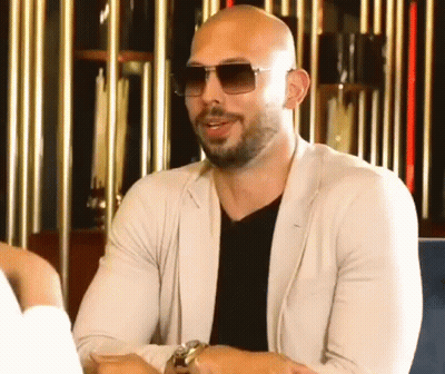 A Bald Man With A Beard And Sunglasses Is Sitting At A Table . GIF