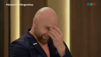 A Bald Man With A Beard Is Covering His Face In Front Of A Masterchef Argentina Logo GIF