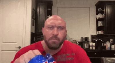 A Bald Man With A Beard Is Eating A Bag Of Potato Chips In A Kitchen . GIF