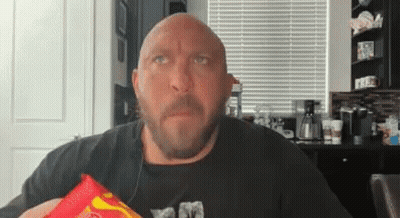 A Bald Man With A Beard Is Holding A Bag Of Chips In His Hand . GIF