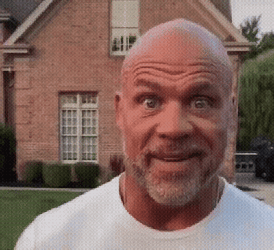 A Bald Man With A Beard Is Making A Face In Front Of A Brick House . GIF