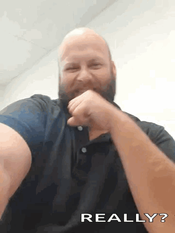 A Bald Man With A Beard Is Making A Funny Face And Covering His Mouth With His Fist . GIF