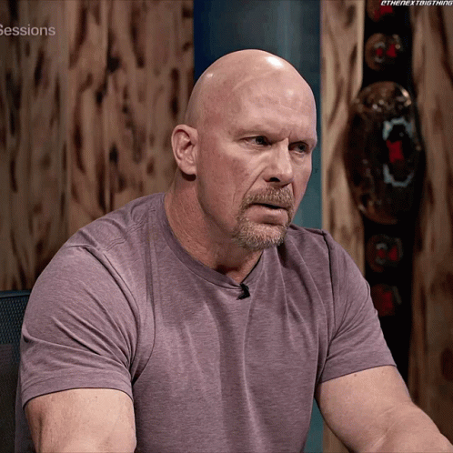 A Bald Man With A Beard Is Sitting In Front Of A Wooden Wall With The Words Sessions On It GIF