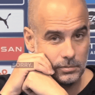 A Bald Man With A Beard Is Sitting With His Hands On His Chin And Looking At The Camera . GIF